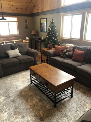 A cozy living room with a wooden coffee table, two sofas, a Christmas tree, and a dining table with chairs.