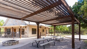 A covered outdoor area with picnic tables and a stone fire pit. - Vacation Home with pool located in Cypress Bend (Concan)