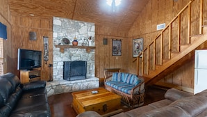 A cozy living room with a stone fireplace, leather sofas, a wooden staircase, and a television. - Vacation Home with pool located in Cypress Bend (Concan)