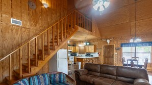 A wooden interior with a staircase, a sofa, a couch, a kitchen area, and a dining table. - Vacation Home with pool located in Cypress Bend (Concan)