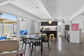 A modern kitchen with dark cabinets, a central island, and a dining area with a glass table and black chairs.