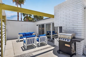 Un patio exterior con pared de ladrillo blanco, una parrilla y mobiliario azul para exteriores.