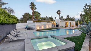 Ein Swimmingpool mit Liegestühlen, einem Whirlpool und einem modernen Haus mit überdachter Terrasse.