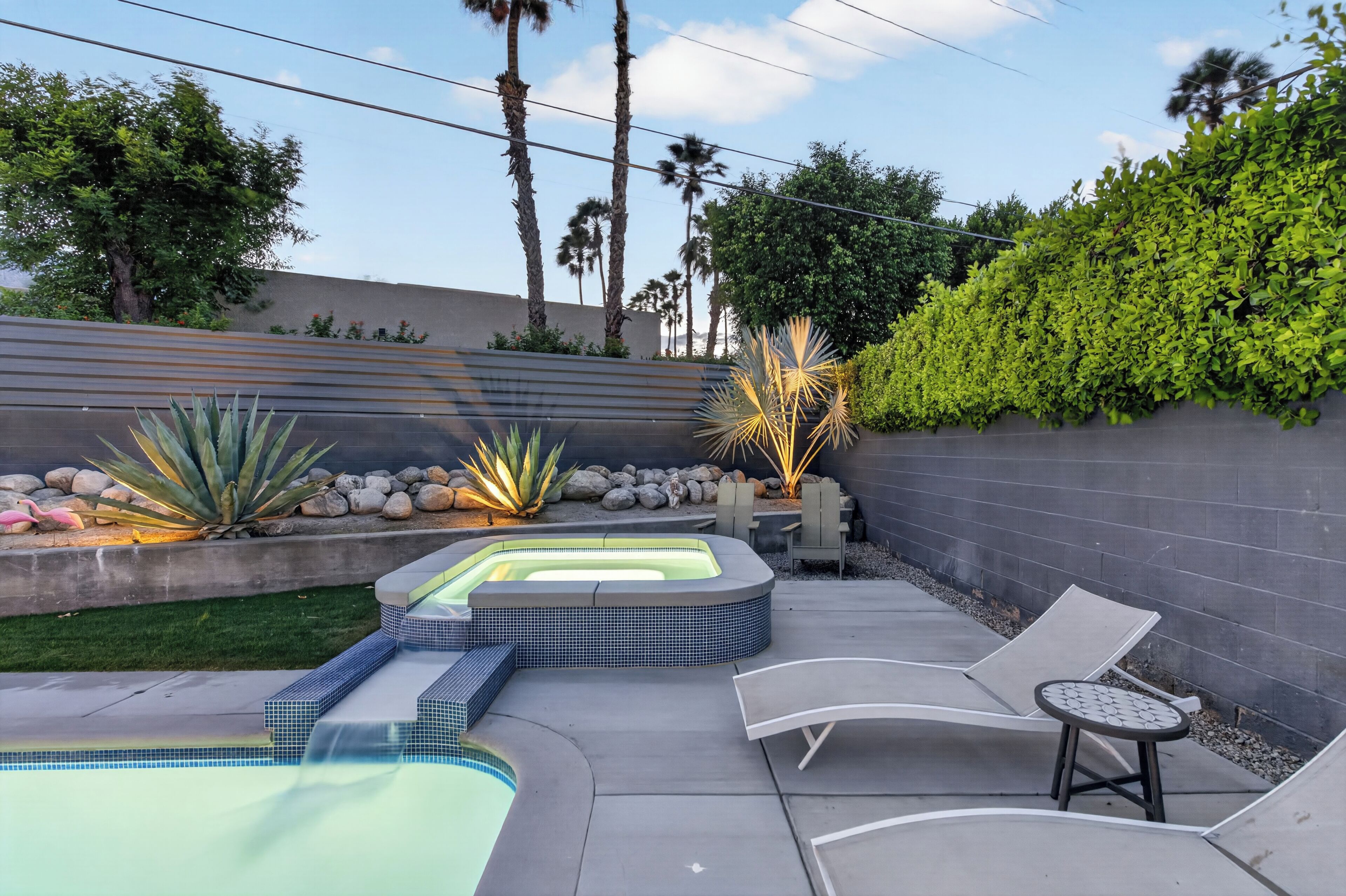 A backyard with a hot tub, lounge chairs, and a small table.