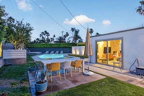 Una casa moderna con piscina, mobiliario exterior y puerta de cristal que da a una sala de estar.