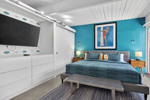 Un dormitorio con una cama grande, un televisor, un cuadro enmarcado y una ventana.