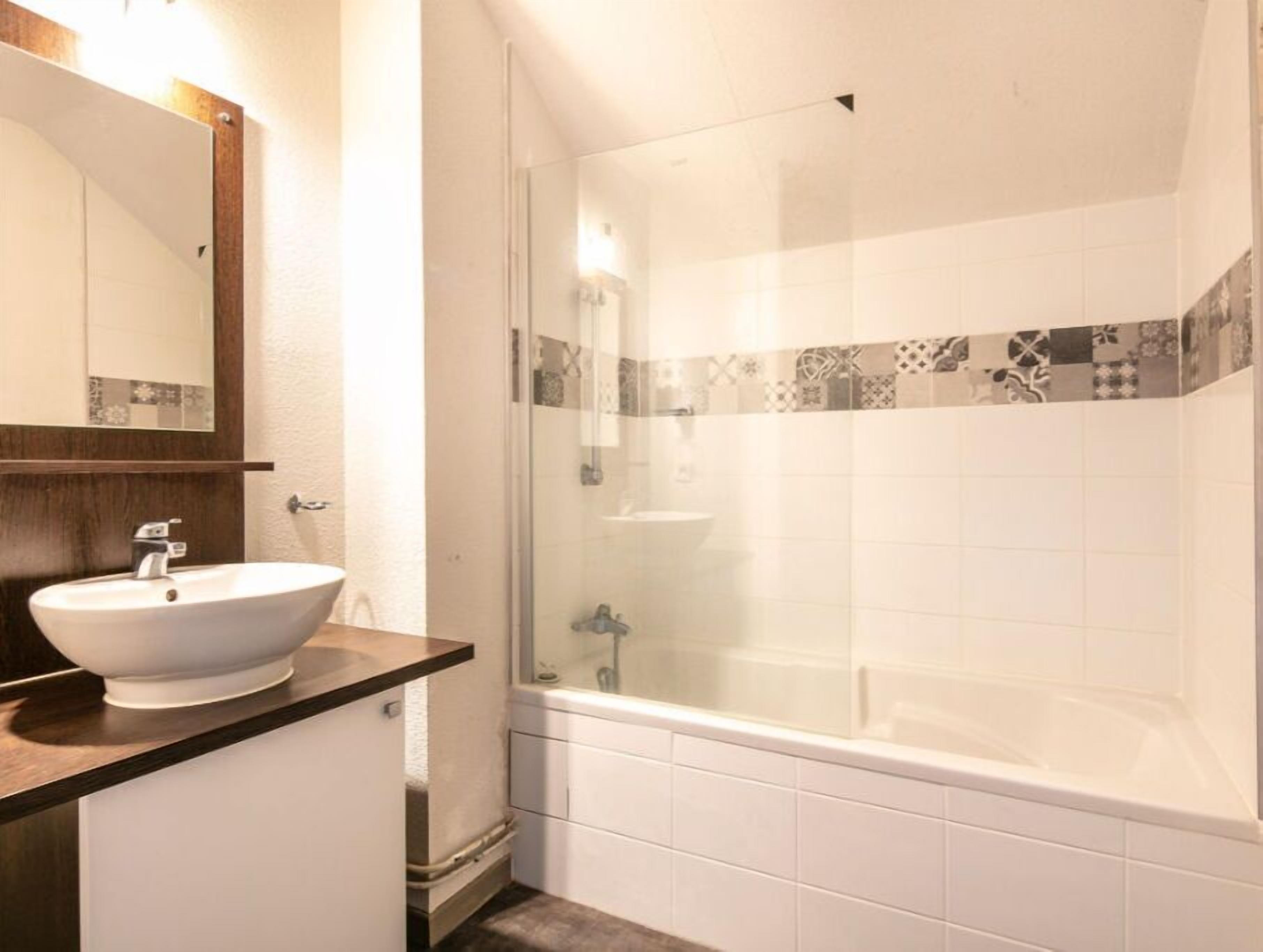Un baño con lavamanos blanco, espejo y cabina de ducha con paredes de vidrio.