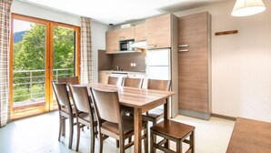 A modern kitchen with wooden cabinets, a dining table with chairs, and a view of greenery outside.
