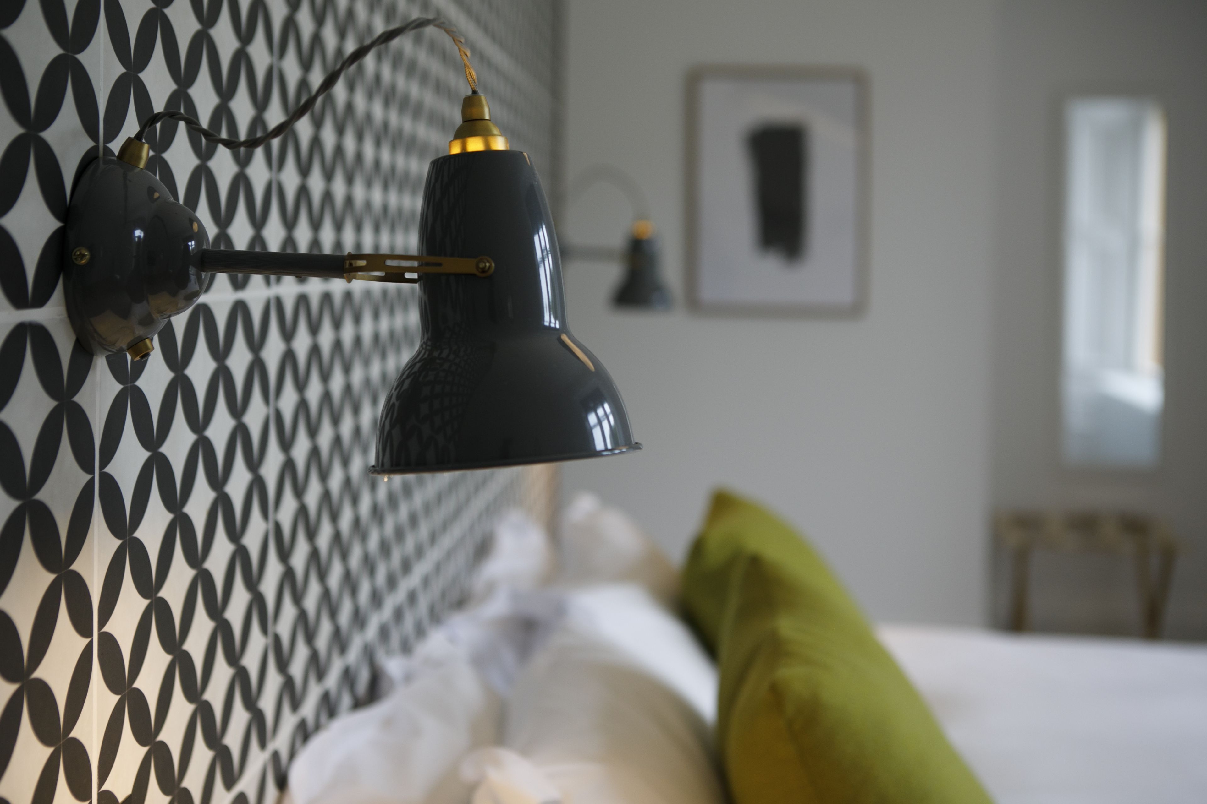 A modern room with a patterned wall, a bed with white bedding, and a black desk lamp.