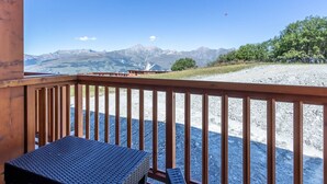 A wooden deck with a table and chairs, overlooking a gravel area with a mountain view.