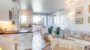 Eine moderne Küche mit weißen Schränken, ein Essbereich mit Tisch und Stühlen sowie ein Wohnzimmer mit Sofa und einem gemusterten Überwurf.