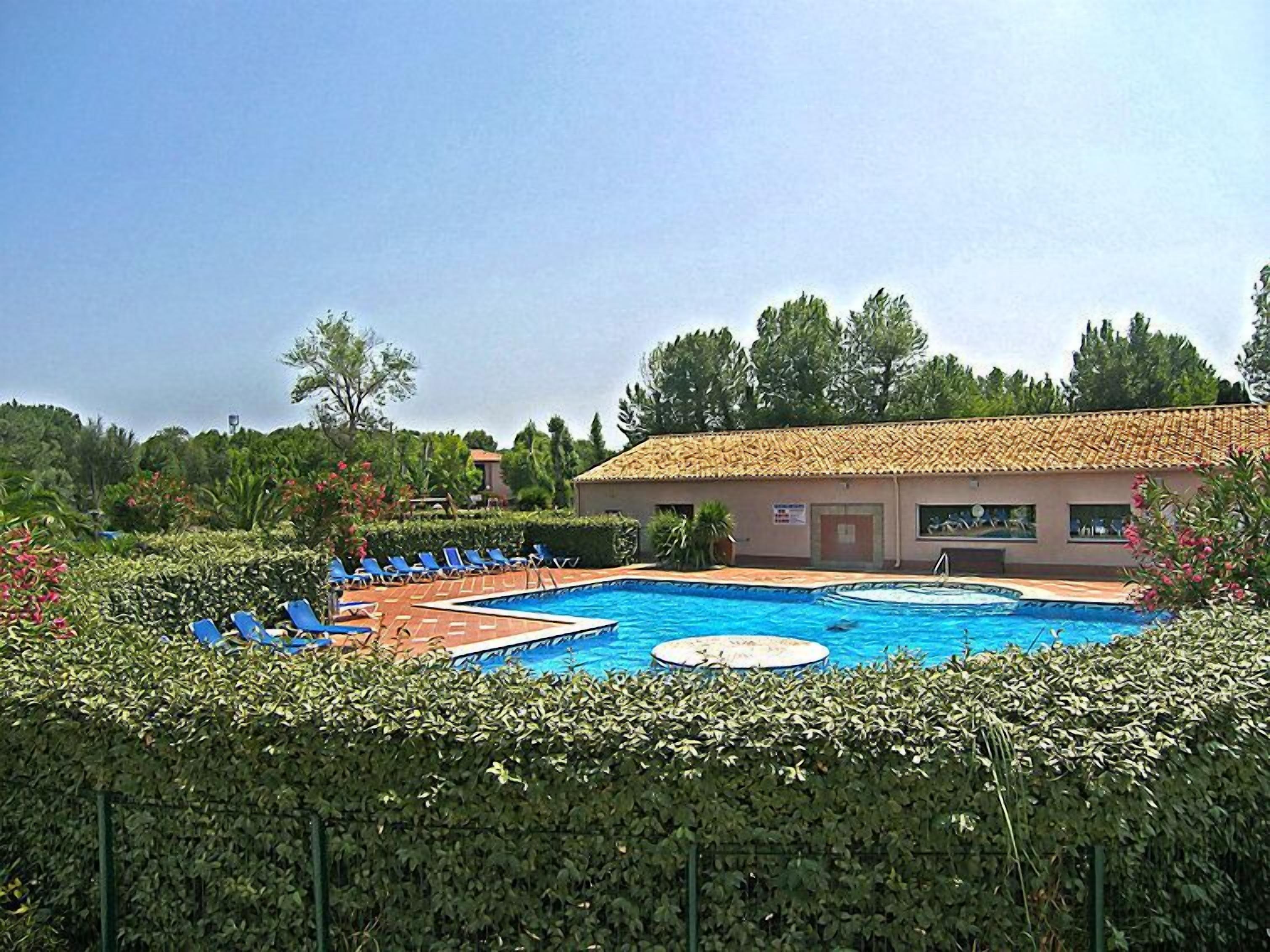 A swimming pool with lounge chairs, surrounded by greenery and a building with a tiled roof.