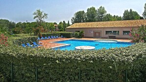 Ein Swimmingpool mit Liegestühlen, umgeben von Grünflächen und einem Gebäude mit Ziegeldach.