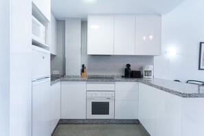 A compact kitchen with white cabinets, a built-in oven, a coffee maker, and a knife block.