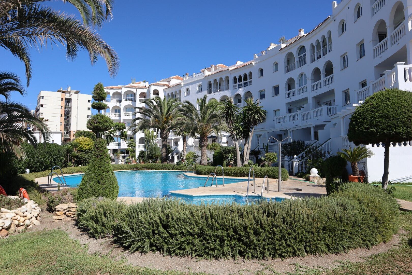 Ett semesterhotell med en swimmingpool, palmer och en vit byggnad med balkonger.