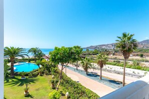 A pool surrounded by palm trees and a view of the ocean and hills.