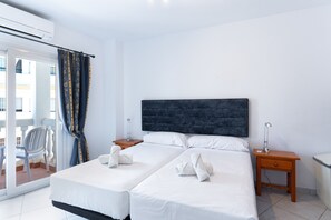 Ein Hotelzimmer mit zwei Betten, einem großen Fenster mit Vorhängen, einem Sessel und einem kleinen Tisch.