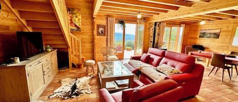 Interior acogedor de una cabaña de madera con un sofá rojo, una mesa de comedor de madera y un televisor sobre un mueble.