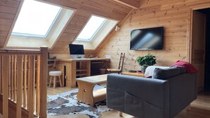 A cozy loft-style room with a wooden interior, a desk with a computer, a couch, and a TV mounted on the wall.