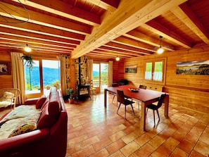 A cozy cabin with a stone fireplace, wooden beams, a dining area, and a sofa.