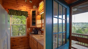Cocina de cabaña con armarios de madera, un fregadero y una ventana con vistas a un bosque.