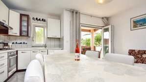 A modern kitchen with white cabinets, a built-in oven, and a dining area with a table and chairs. - Beautiful apartment for 6 guests with WIFI, pool, A/C, TV and terrace (Zadar)