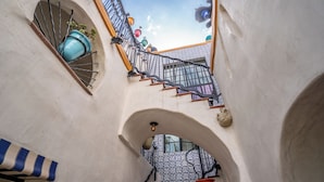 A narrow stairway with a metal railing, leading to a higher level. There are decorative elements like a blue vase and a red pot on the walls. - Iconic, Unique Home in the Heart of Downtown SB! (Santa Barbara)
