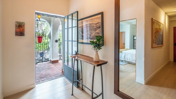 A hallway with a wooden floor, a mirror, a potted plant, and artwork on the walls. - Iconic, Unique Home in the Heart of Downtown SB! (Santa Barbara)