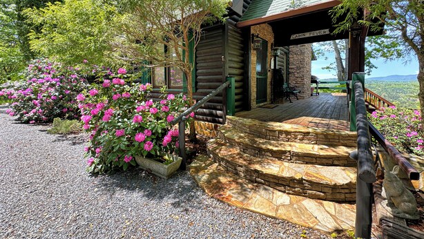 Uma cabana com base de pedra, deck de madeira e varanda com escadaria de pedra.