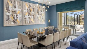 A modern dining area with a glass table, beige chairs, and abstract art on the wall. - Fun Home Near Disney w/ Princess & Space BRs, Arcade, Game Loft, Theater & Pool (Davenport)