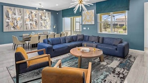 A modern living room with a sectional sofa, a round coffee table, and a dining area with chairs. - Fun Home Near Disney w/ Princess & Space BRs, Arcade, Game Loft, Theater & Pool (Davenport)