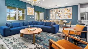 A modern living room with a blue sectional sofa, a round coffee table, and a dining area with a white table and chairs. - Cozy Home Near Parks w Toy & BBall Theme BRs, Theater, Arcade, Game Loft, Pool (Davenport)