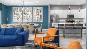 A modern living room with a blue sofa, orange chairs, and abstract art on the wall. - Cozy Home Near Parks w Toy & BBall Theme BRs, Theater, Arcade, Game Loft, Pool (Davenport)