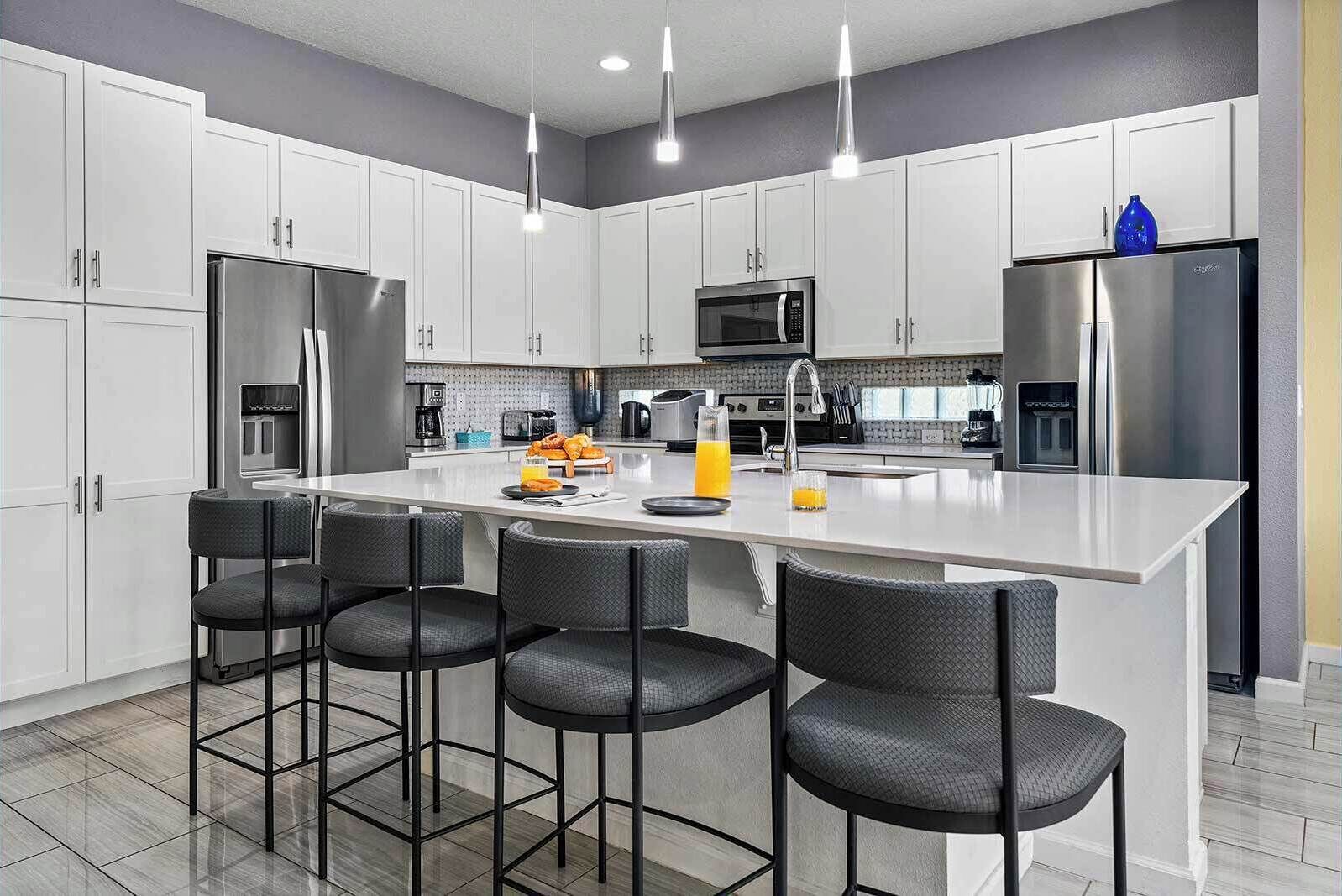 A modern kitchen with white cabinets, stainless steel appliances, a central island with bar stools, and pendant lighting.