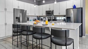 A modern kitchen with white cabinets, stainless steel appliances, a central island with bar stools, and pendant lighting. - Unreal Home Near Disney w/ Volcano & Space Theme BRs, Theater, Arcade, Game RM (Davenport)