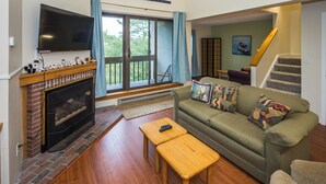 Una sala de estar con chimenea, televisor, sof á y escalera.