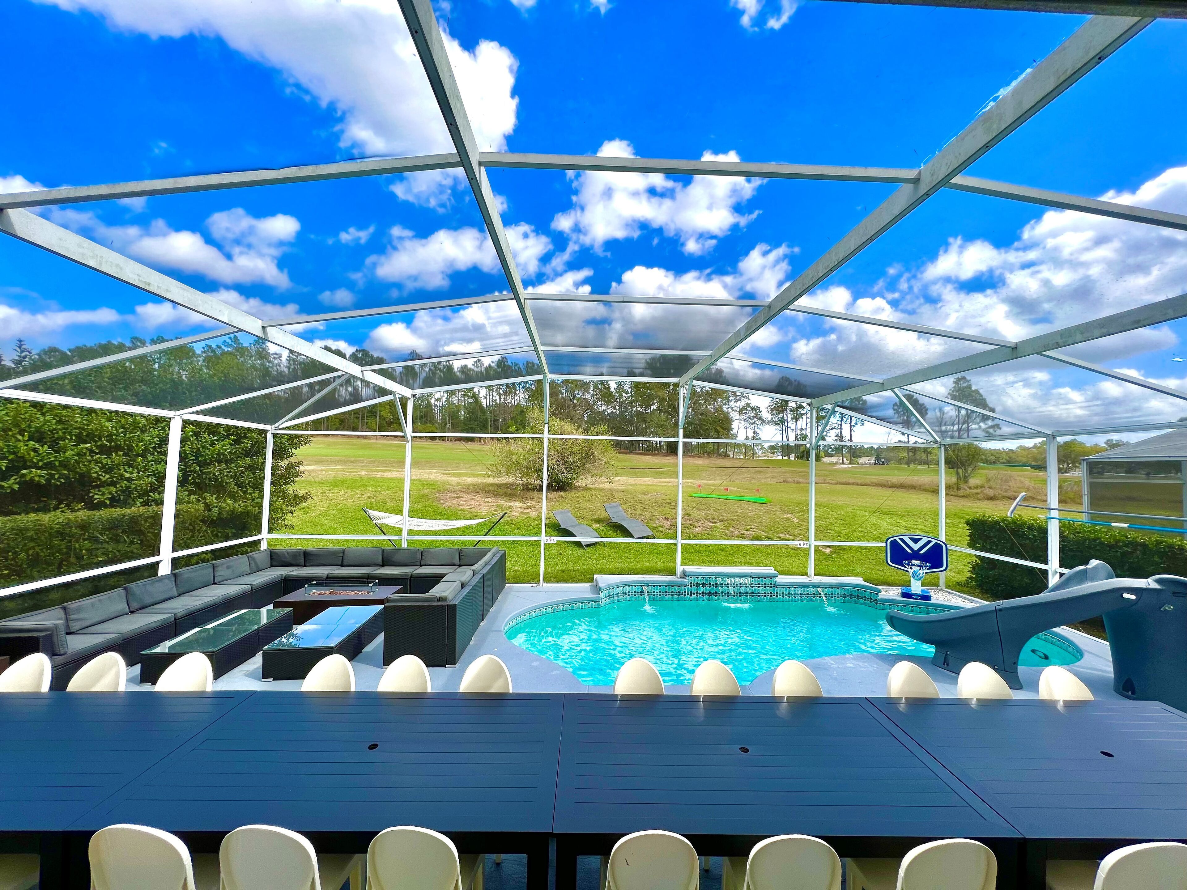 A covered outdoor area with a pool, seating, and a view of a golf course.