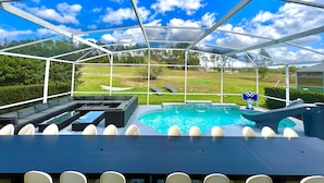 A covered outdoor area with a pool, seating, and a view of a golf course. - 14 room DisneyEstate by AmericanVacationLiving (Davenport)