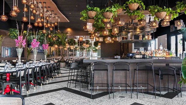 A restaurant with multiple dining tables, hanging plants, and a bar area. - 14 room DisneyEstate by AmericanVacationLiving (Davenport)