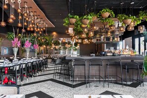 A restaurant with multiple dining tables, hanging plants, and a bar area. - 14 room DisneyEstate by AmericanVacationLiving (Davenport)
