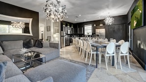 A modern living room with a large gray sofa, a glass coffee table, and a dining area with white chairs and a long table. - 14 room DisneyEstate by AmericanVacationLiving (Davenport)
