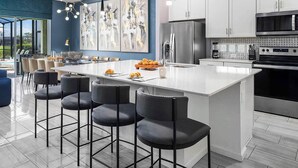 Una cocina moderna con una isla central, taburetes de bar, electrodomésticos de acero inoxidable y un cuadro abstracto grande en la pared.