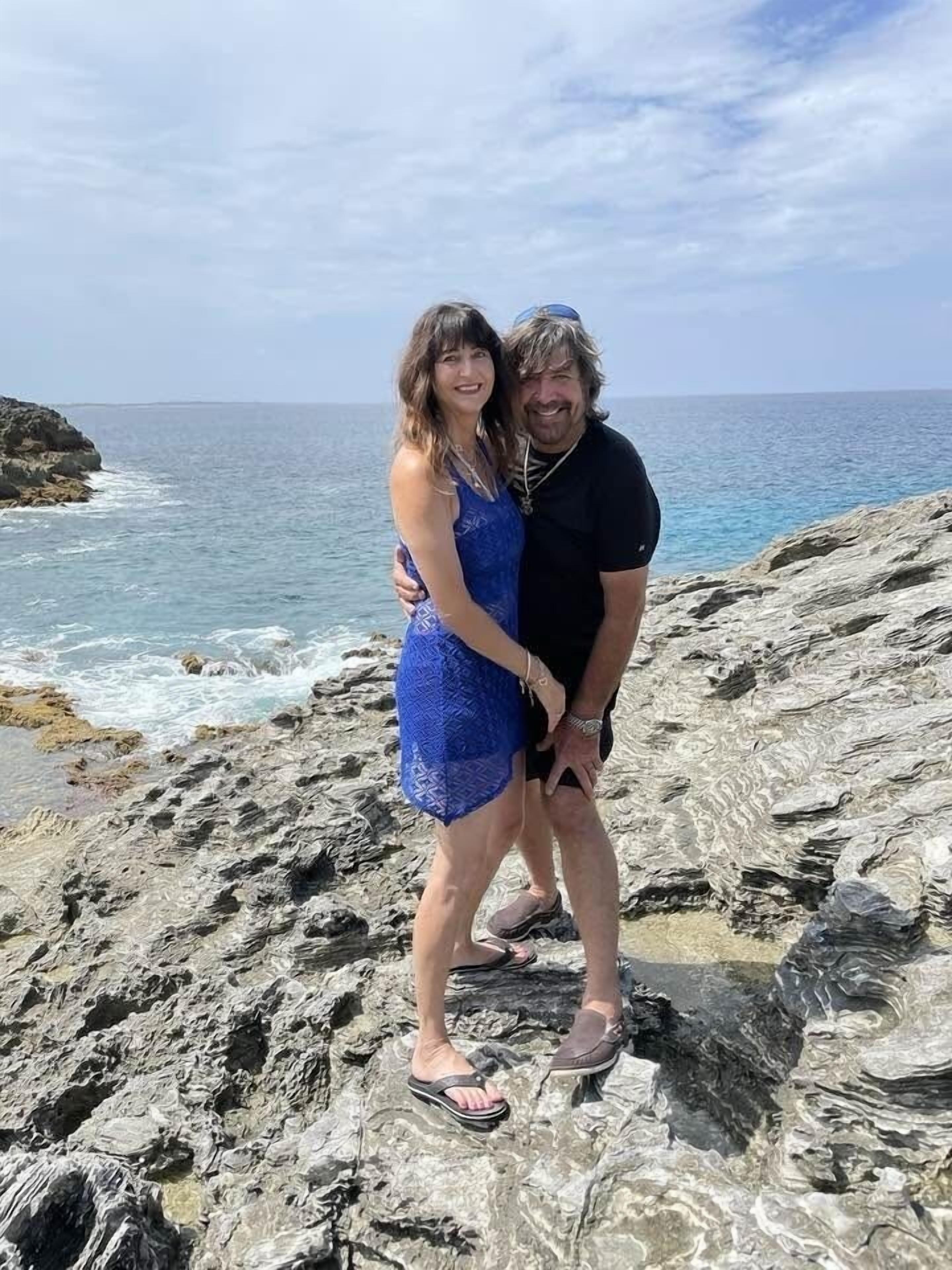 Una pareja parada sobre terreno rocoso con vista al océano.