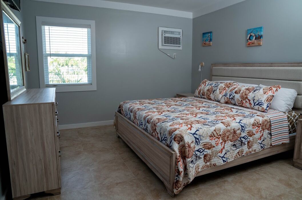 A bedroom with a bed, a dresser, a window, and an air conditioning unit.