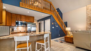 Eine moderne Küche mit Holzausbau, einem Edelstahlkühlschrank und einer Marmorarbeitsplatte. Eine Holztreppe führt zu einer zweiten Etage.