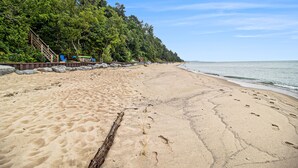 Ein sandiger Strand mit einer Holztreppe, die zu einer Terrasse führt, umgeben von Bäumen.