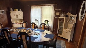 A dining area with a wooden table, chairs, a ceiling fan, and a cabinet with glass doors. - Pappys place at Smoke Hole (Upper Tract)