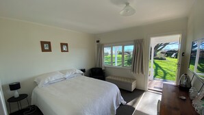 A bedroom with a bed, bedside table, lamp, window, and a view of a garden.