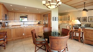 A spacious kitchen with wooden cabinets, a central island, and a dining area with wicker chairs and a glass table.