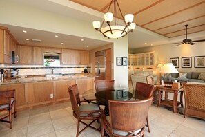 A spacious kitchen with wooden cabinets, a central island, and a dining area with wicker chairs and a glass table.